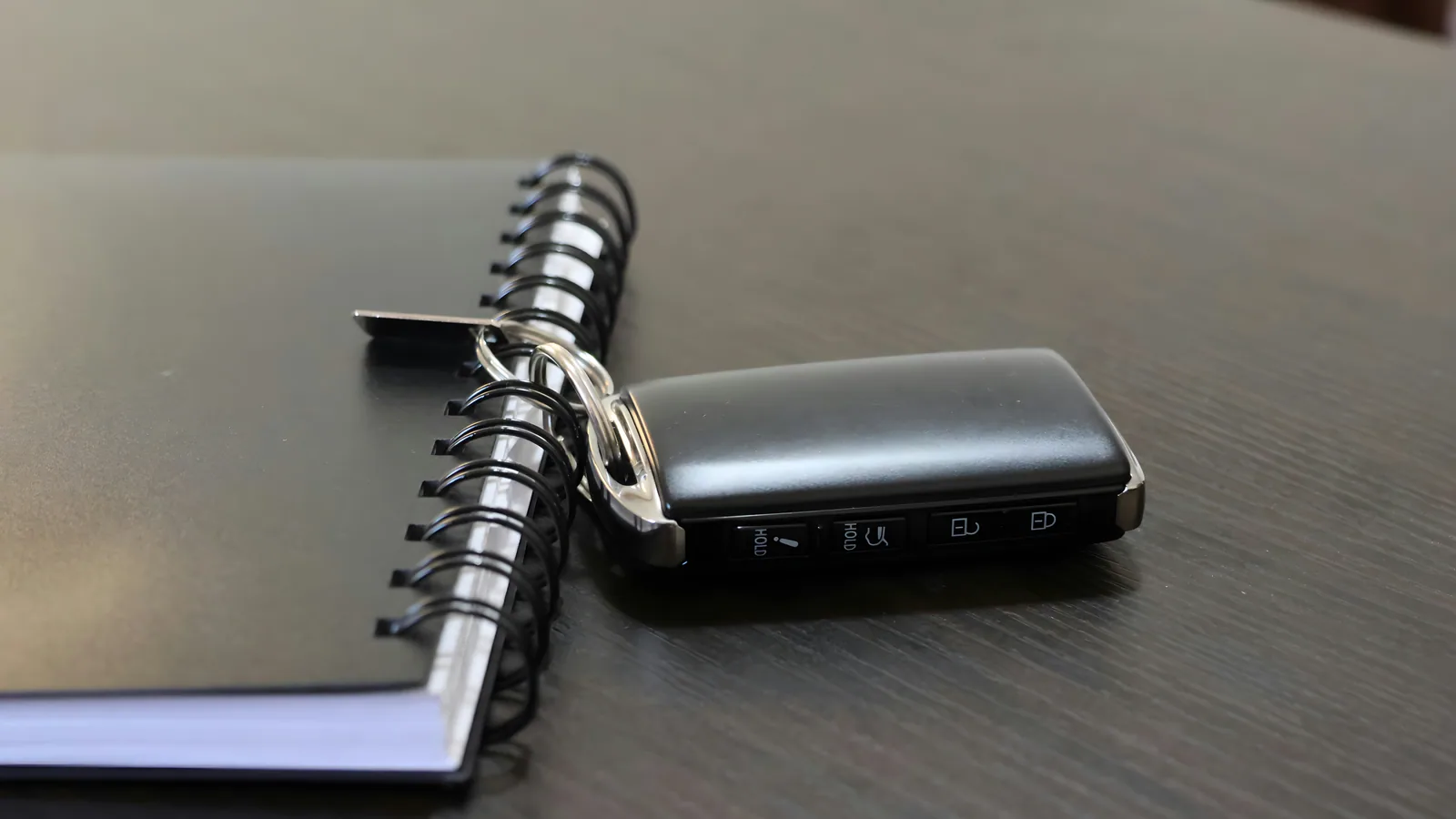 A car key resting on a notebook on a wooden desk.